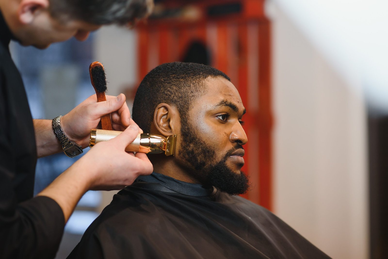 Portrait of young black man being trimmed with professional electric clipper machine in barbershop.Male beauty treatment concept. Young African guy getting new haircut in barber salon